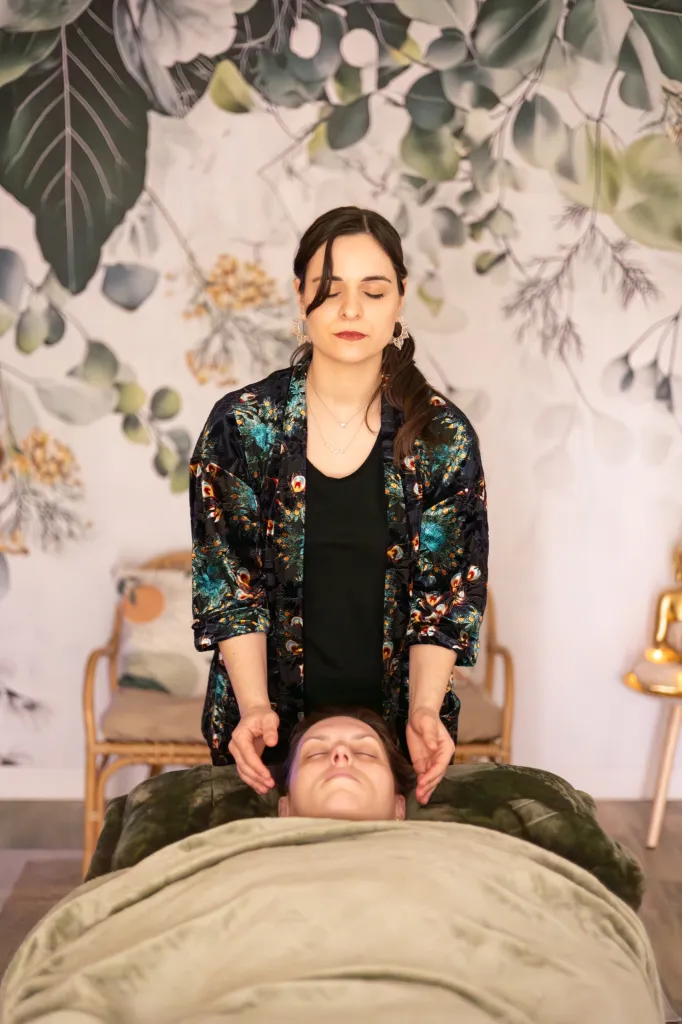 Sarah pendant un soin énergétique, les mains près du visage d'une cliente allongée